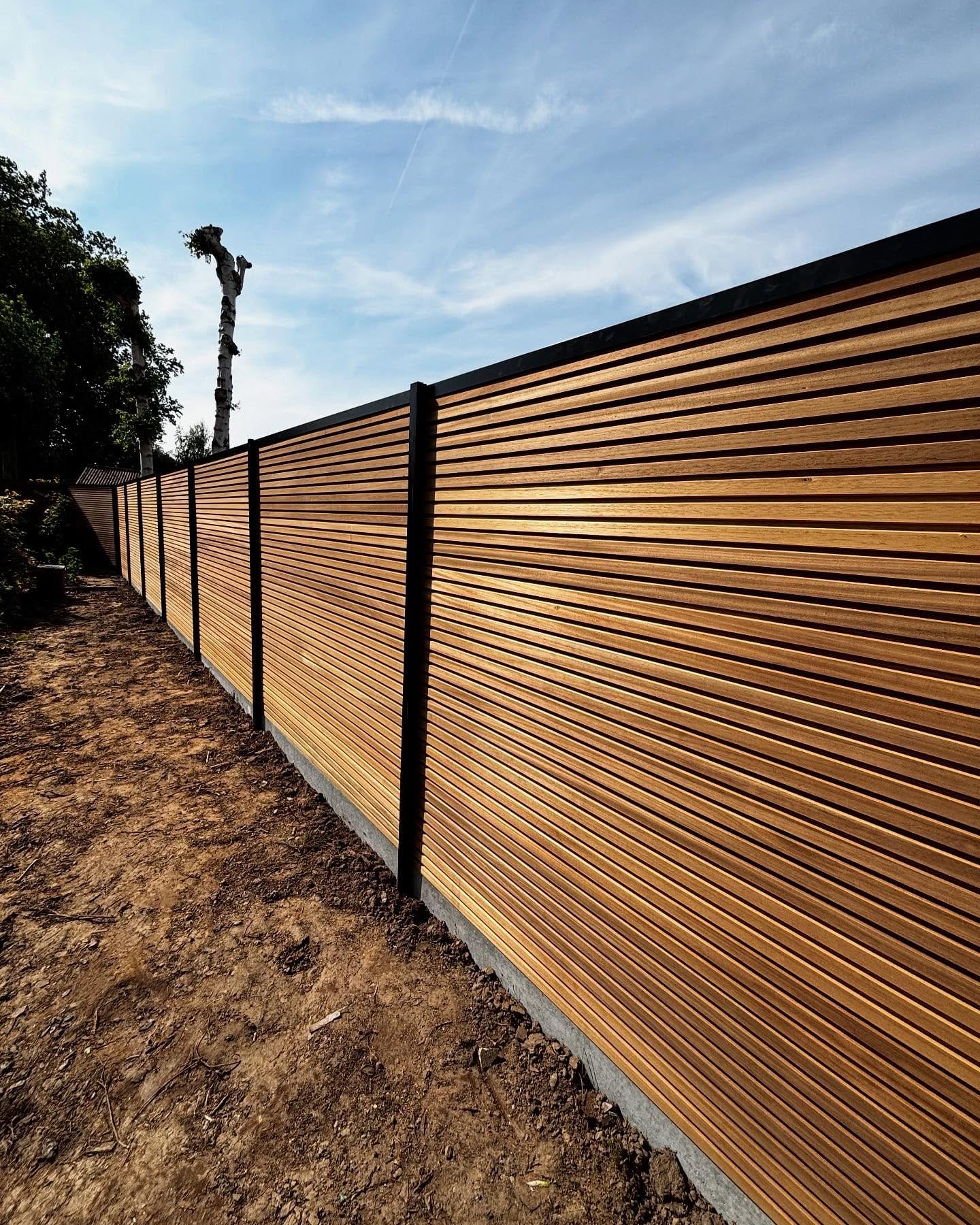 Moderne houten afsluiting met zwarte palen langs een tuin